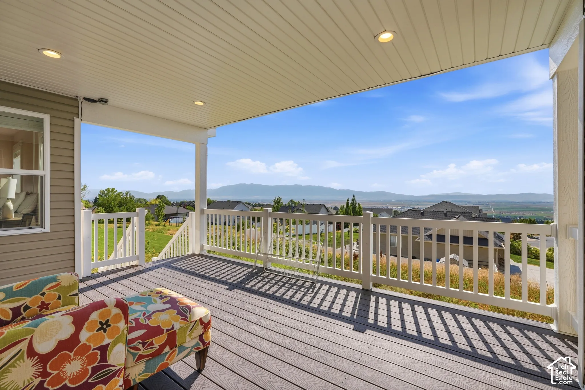 Spacious covered deck featuring composite decking, white railing, recessed lighting, and a distant mountain backdrop