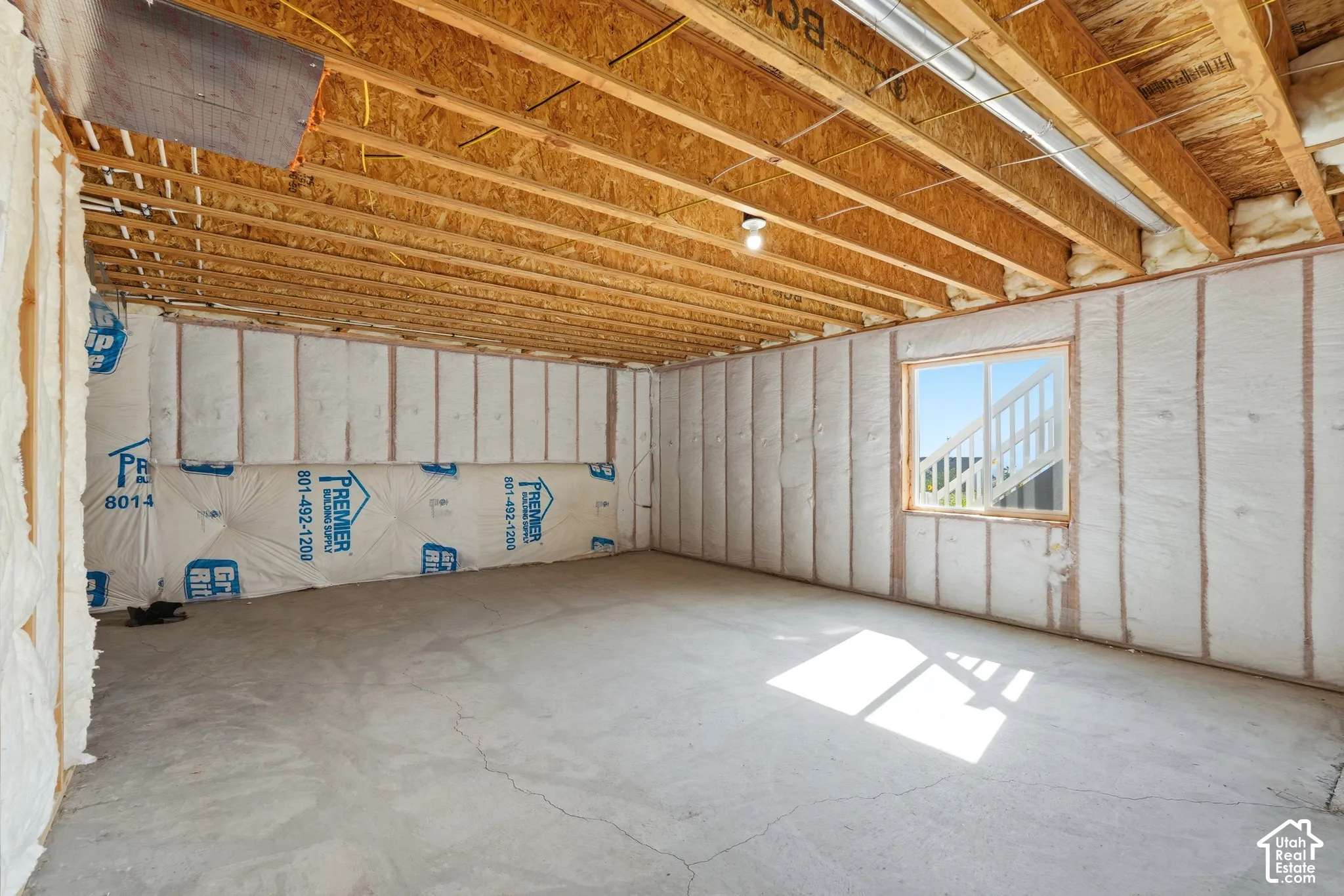 Unfinished interior space featuring exposed ceiling joists, insulated walls, concrete flooring, and a single window
