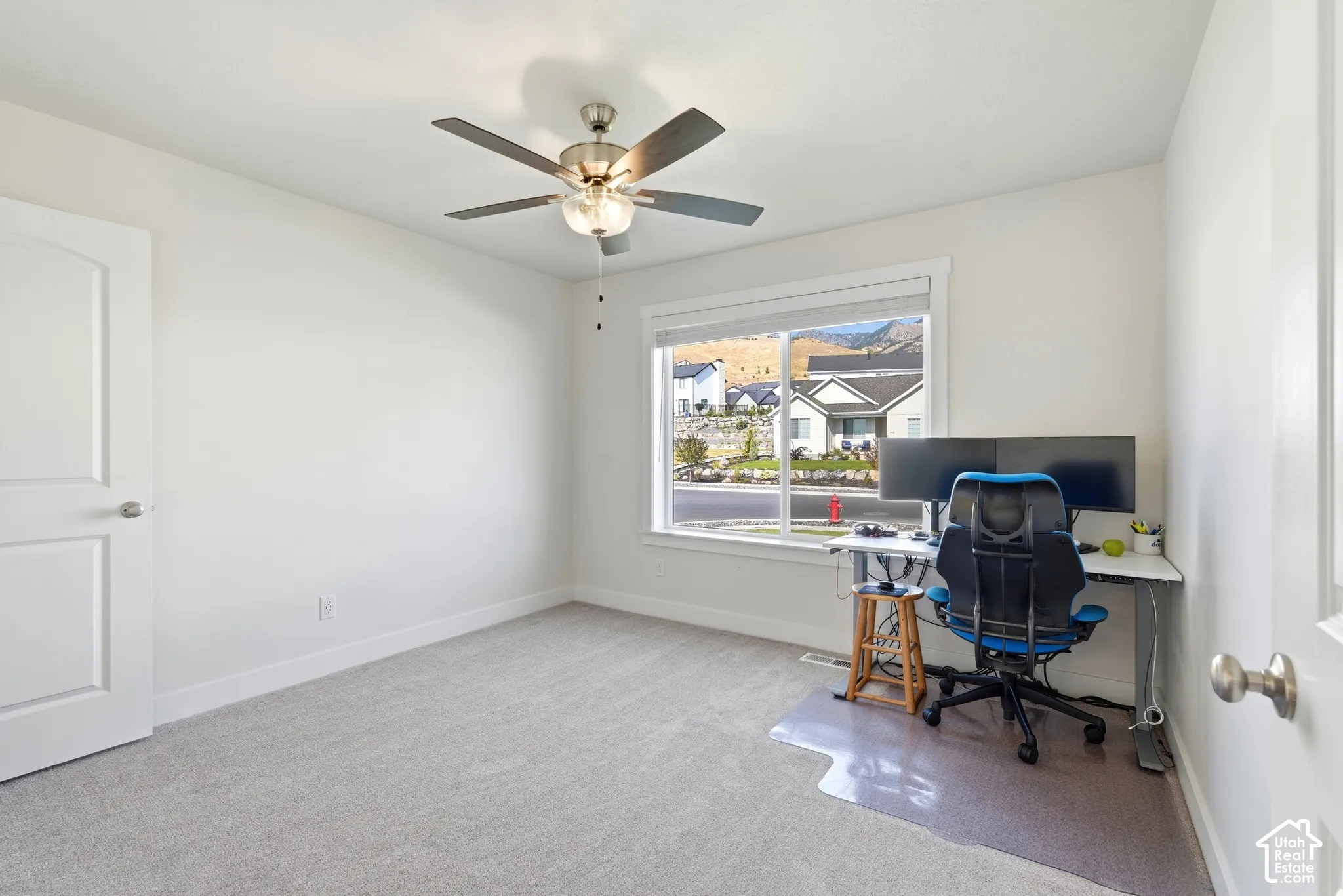 Bright room featuring a ceiling fan, light-colored carpeting, white trim, and a window with a mountain backdrop