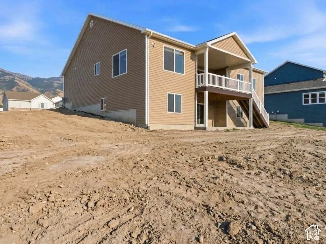 Tan horizontal siding with white trim, covered balcony with white railing, exterior stairs with white railing, lower level exterior door, and multiple windows