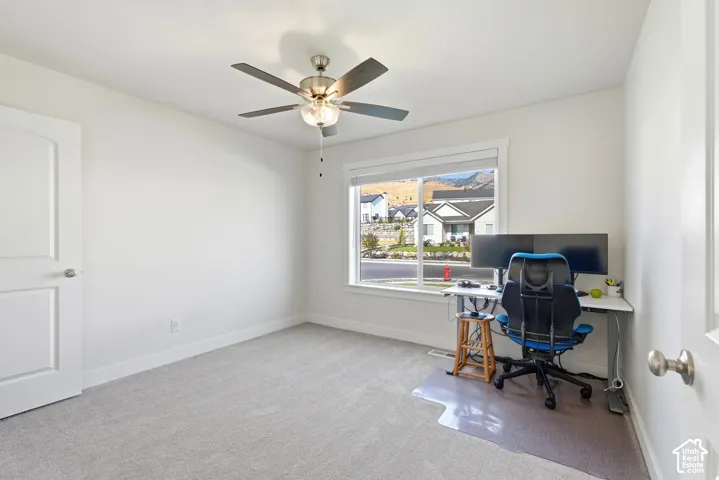 Bright room featuring a ceiling fan, light-colored carpeting, white trim, and a window with a mountain backdrop