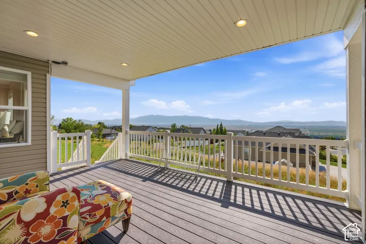 Spacious covered deck featuring composite decking, white railing, recessed lighting, and a distant mountain backdrop