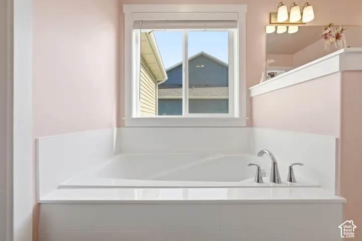 Built-in soaking tub with deck-mounted chrome fixtures, surrounded by white tile and a window with trim