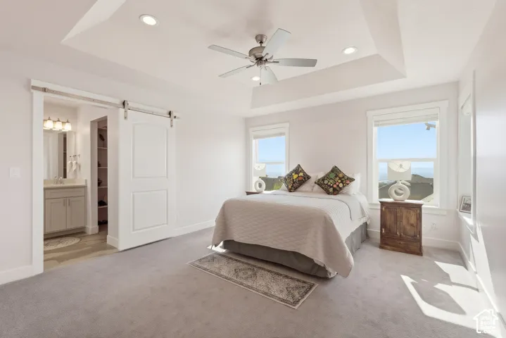 Tray ceiling with recessed lighting, central ceiling fan, and white sliding barn door