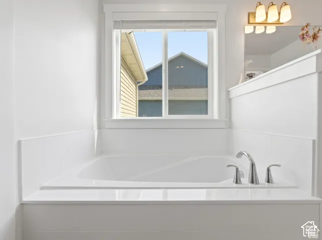 Built-in soaking tub with white tile surround, chrome deck-mounted faucet, and polished surface, featuring a window and three-light vanity fixture