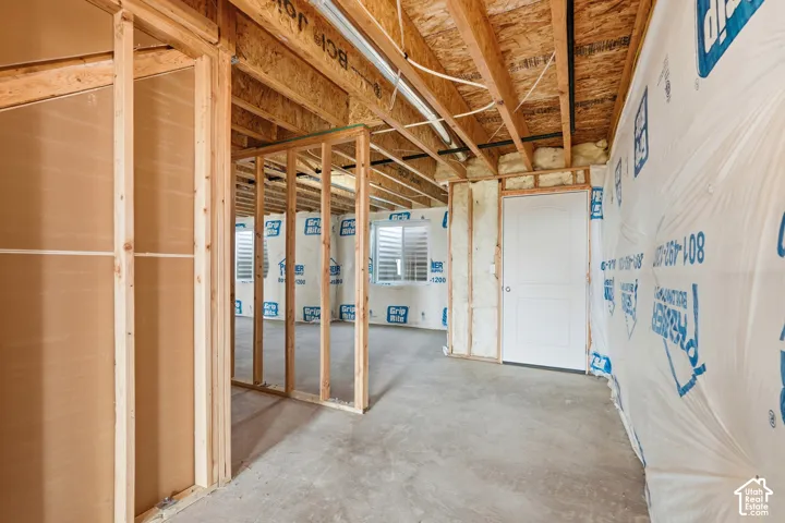 Unfinished basement featuring exposed wood framing, concrete flooring, and a paneled interior door