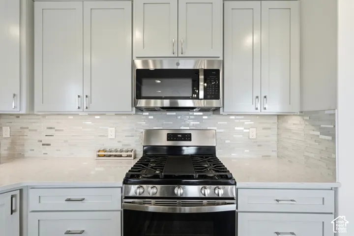 Stainless steel gas range with coordinating microwave, light-toned cabinetry with modern hardware, quartz countertops, and a mosaic tile backsplash