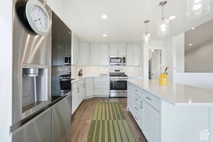 Kitchen featuring light-toned cabinetry, stainless steel appliances, white subway tile backsplash, and a large central island with a light-colored countertop