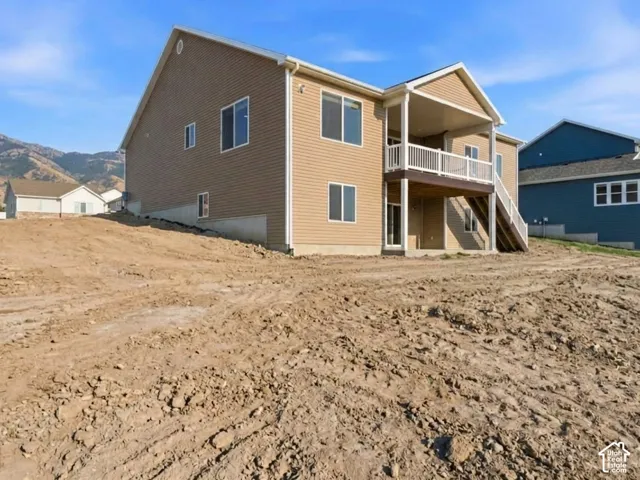 Tan horizontal siding with white trim, covered balcony with white railing, exterior stairs with white railing, lower level exterior door, and multiple windows