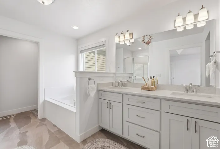Dual-vanity cabinetry with stone-finish countertops, undermount sinks, full-width vanity mirror, drop-in soaking tub, and large-format tile flooring