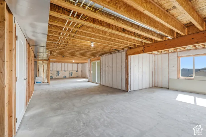 Unfinished basement with exposed wooden joists, concrete flooring, insulated walls, and a visible window