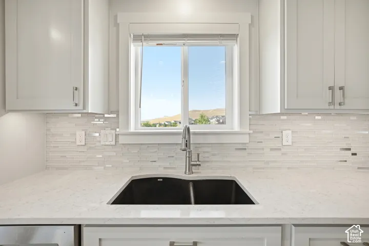 White shaker-style cabinetry with chrome hardware, horizontal tile backsplash, light-toned countertop, and undermount double basin sink with a gooseneck faucet