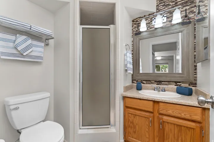 Bathroom featuring a neutral palette, a glass-enclosed shower, a vanity with wood-finish cabinetry, a framed mirror, and a tile backsplash