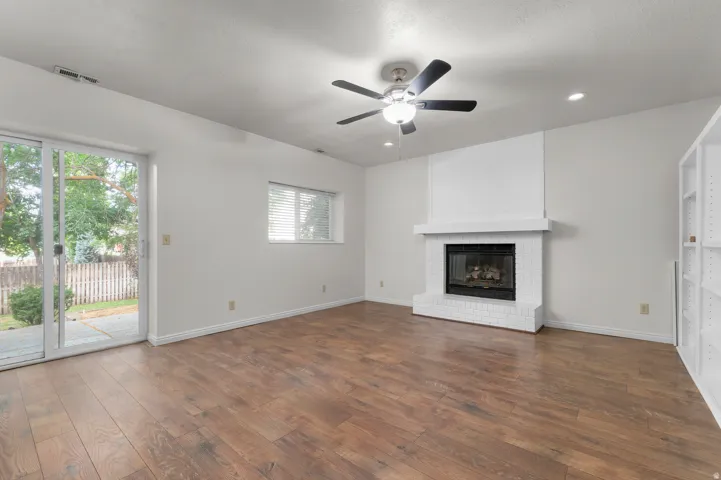 Spacious living area featuring wood-finish flooring, a white brick fireplace with mantel, and built-in shelving