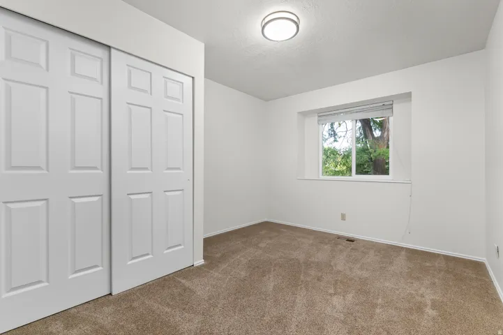 Recessed window, white trim, sliding panel closet doors, flush mount ceiling light, and carpet flooring