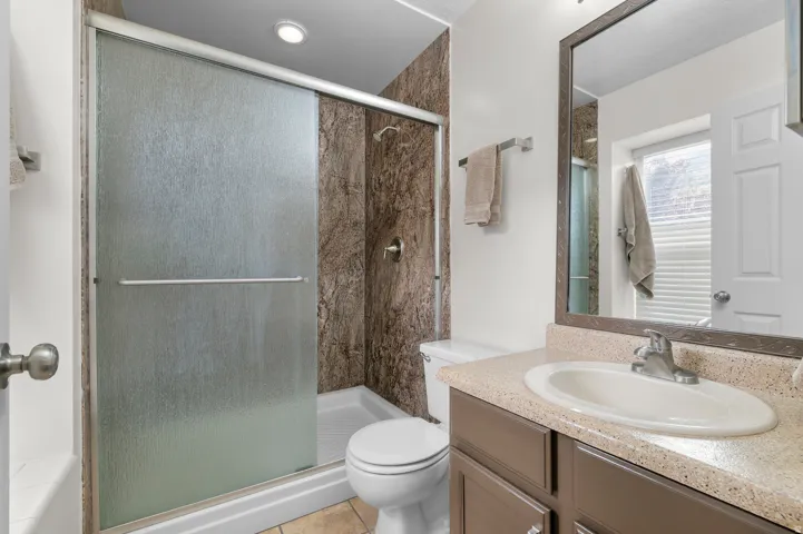 Shower with frosted glass enclosure, brown-toned shower surround, single vanity with integrated sink, and framed wall mirror