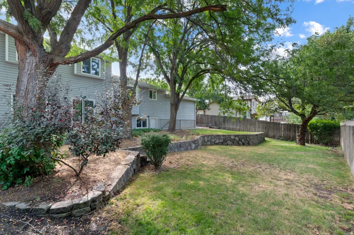 Expansive backyard featuring a stone-faced retaining wall, mature trees, and a wood privacy fence