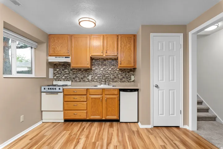 Compact kitchen featuring wood-finish flooring, wood cabinetry, built-in range, built-in dishwasher, and a patterned tile backsplash