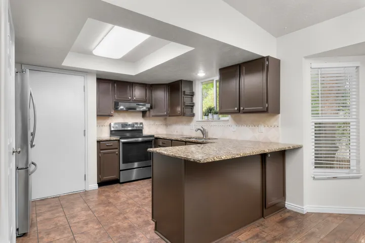 Kitchen featuring stone countertops, dark wood-finish cabinetry, stainless steel appliances, and a tiled backsplash