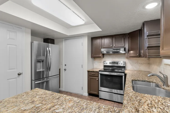 Kitchen featuring granite-style countertops, dark wood-finish cabinetry, a stainless steel range, and a stainless steel refrigerator