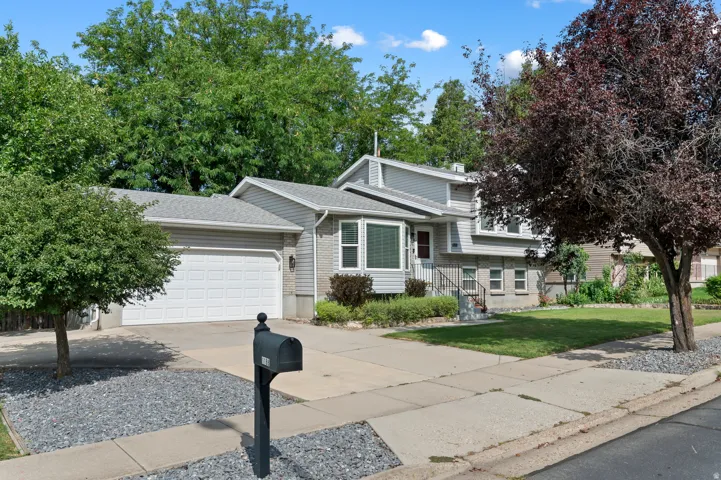 Split-level residence featuring gray siding, a two-car garage, bay window, and mature landscaping