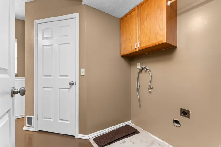 Laundry area with wood-finish upper cabinetry, utility hookups, and a white paneled door