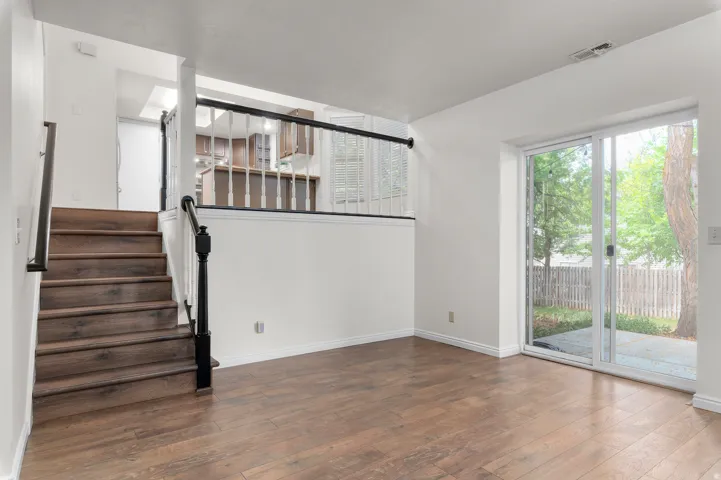 Wood-finish flooring throughout, a staircase with dark wood-finish treads and white risers, a black and white baluster railing, a sliding glass door, and a private outdoor patio