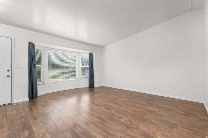 Wood-finish flooring throughout, bright white walls, and a large bay window with horizontal blinds