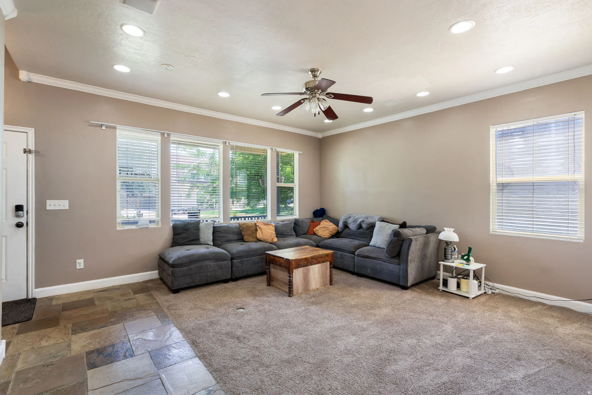 Recessed lighting, ceiling fan, crown molding, multiple windows with blinds, and a combination of tile and carpet flooring
