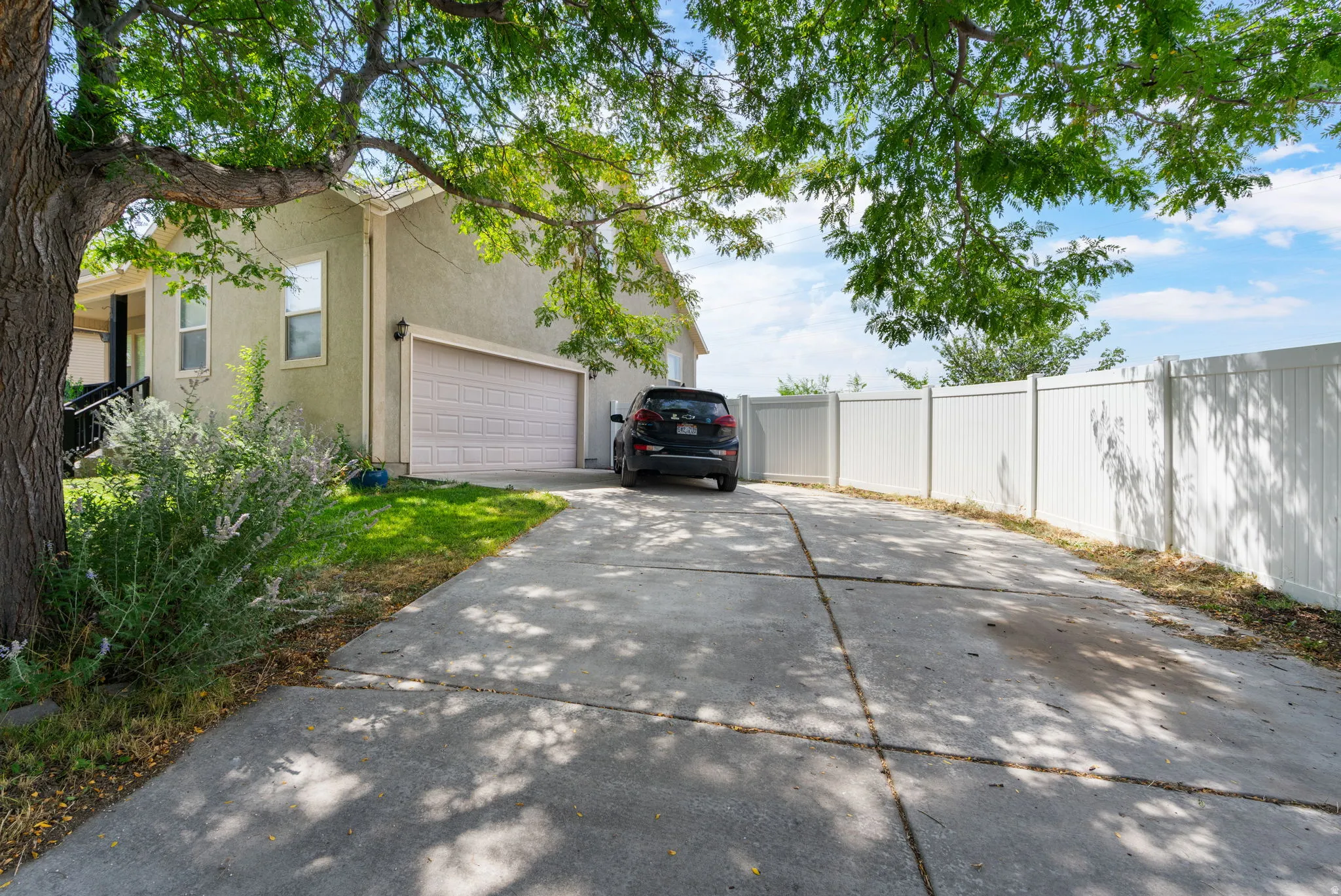 Concrete driveway leading to an attached garage, featuring a light-colored exterior and a white privacy fence