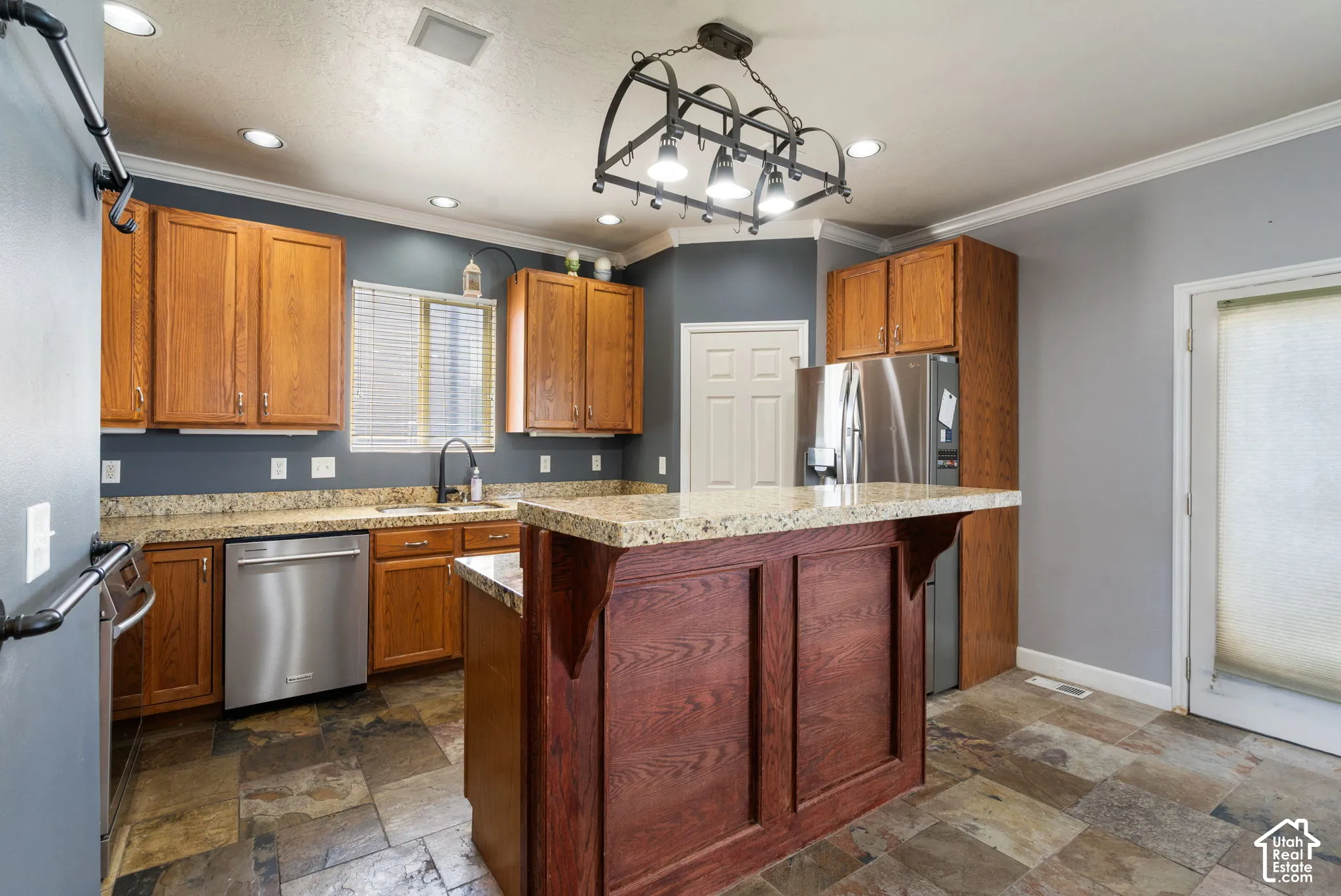 Kitchen featuring stone-look flooring, stainless steel appliances, wood cabinetry, granite countertops, and a central island with paneling