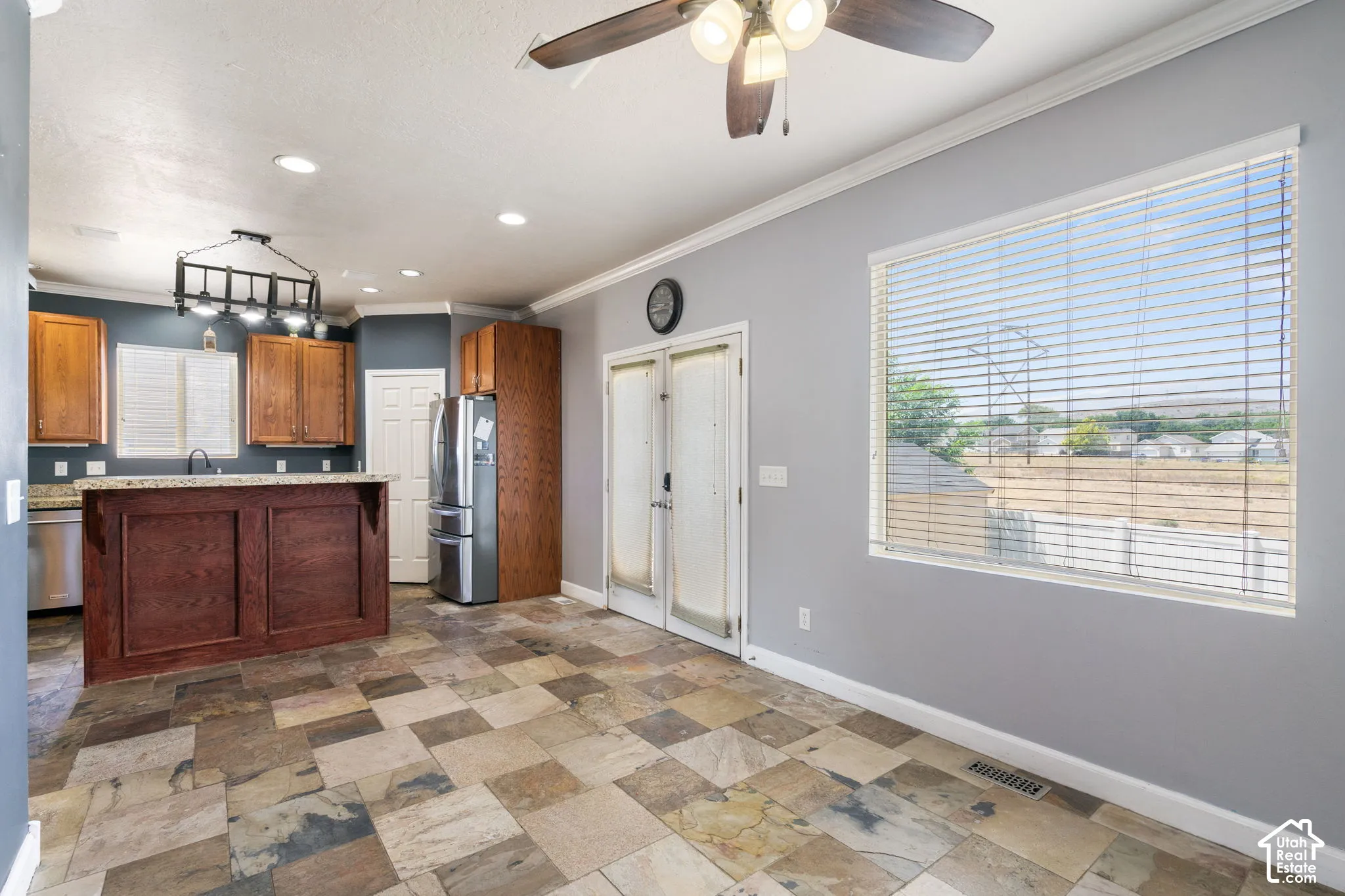 Spacious kitchen and dining area featuring stone tile flooring, a large island with a granite-style countertop, wood cabinetry, and stainless steel appliances