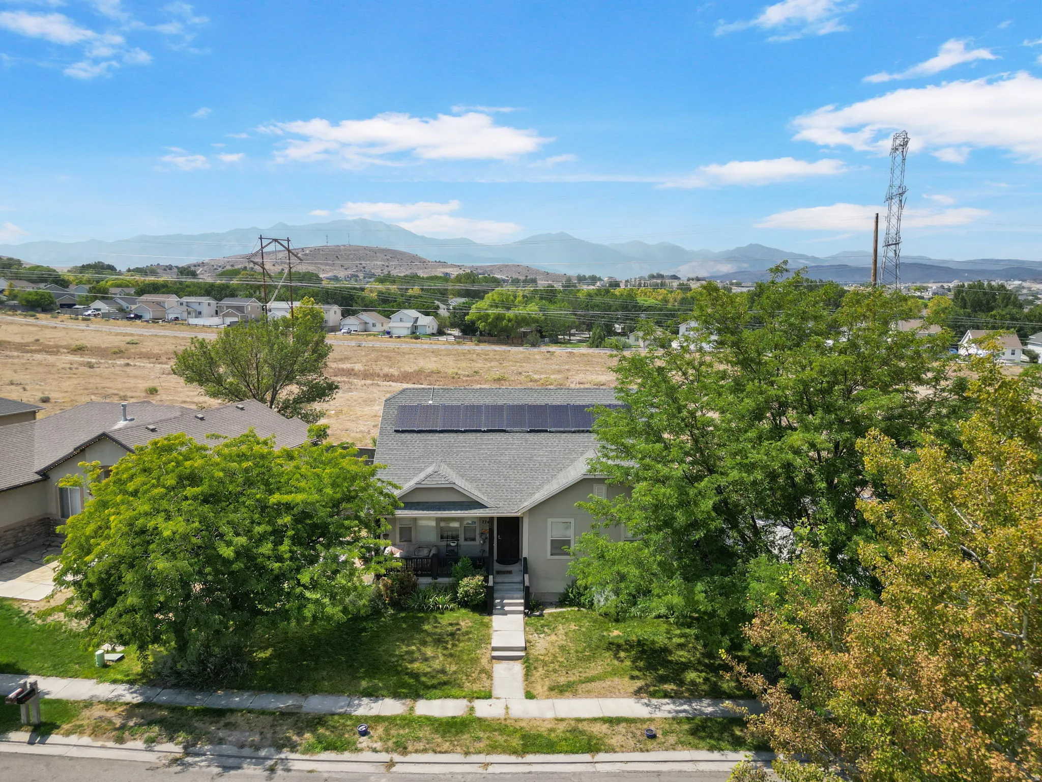 Gabled roofline with solar panels, mature front yard trees, and a concrete walkway