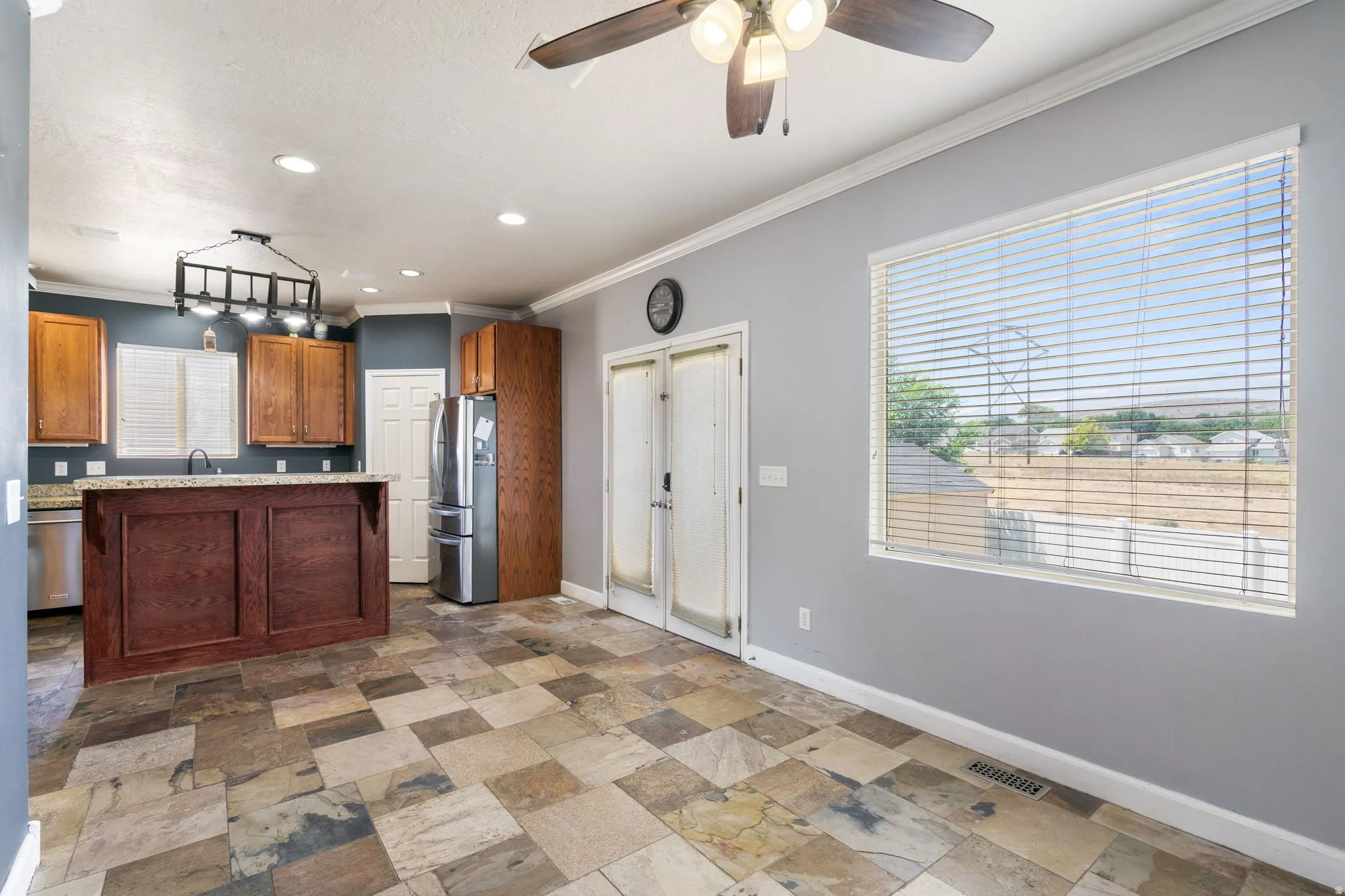 Spacious kitchen and dining area featuring stone tile flooring, a large island with a granite-style countertop, wood cabinetry, and stainless steel appliances