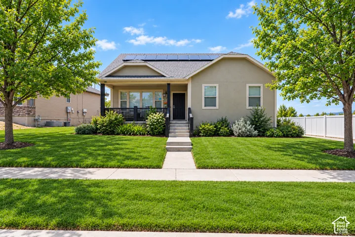 Single-story exterior featuring a covered front porch, low-maintenance stucco siding, solar panels, mature landscaping, and a concrete walkway