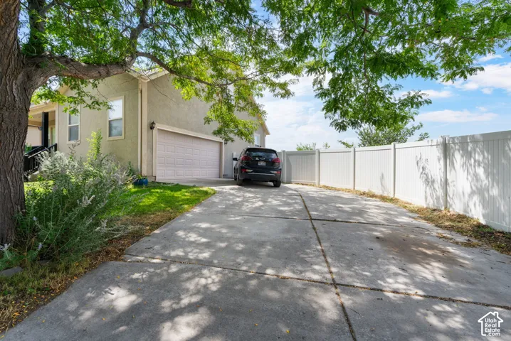 Concrete driveway leading to an attached garage, featuring a light-colored exterior and a white privacy fence