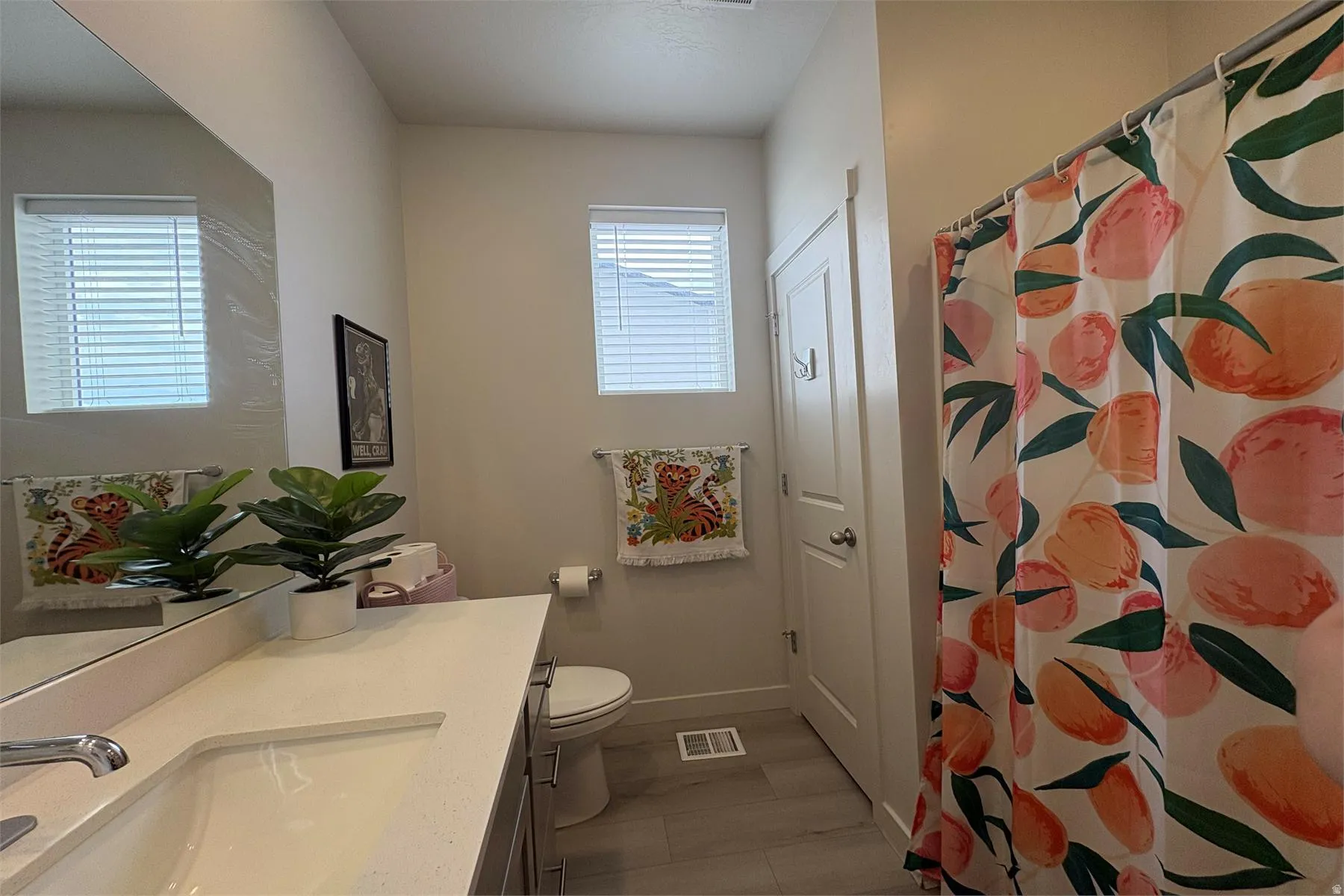 White single vanity with integrated sink, rectangular mirror, and light wood-finish flooring