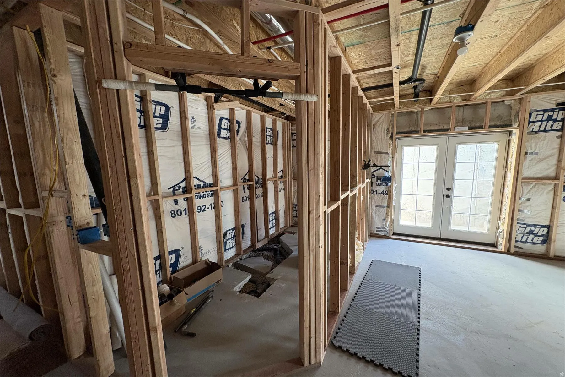 Framed interior space with exposed ceiling joists, concrete flooring, and double French doors with grid-patterned glass