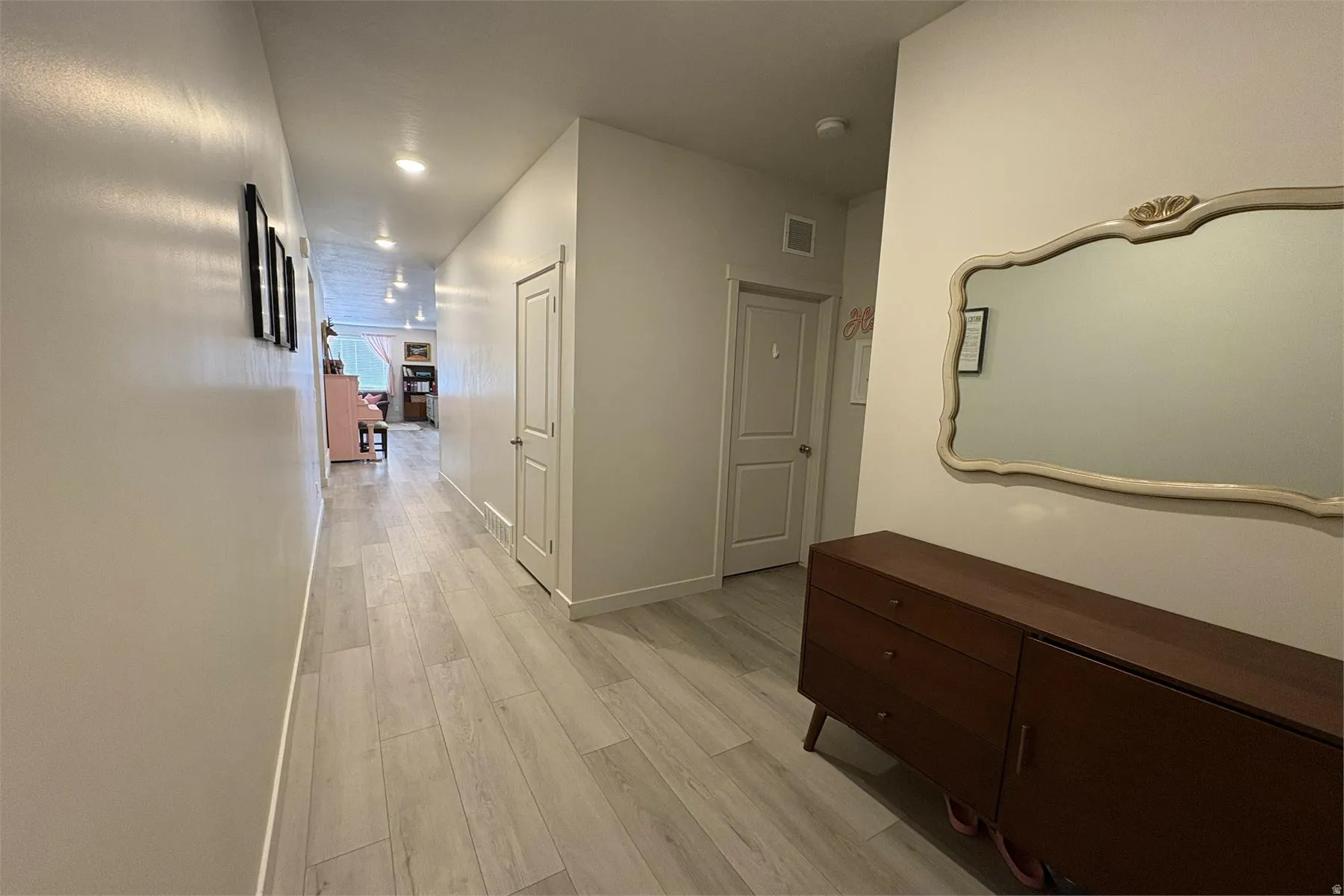 Recessed lighting illuminates the hallway, featuring light wood-finish flooring and multiple paneled doors