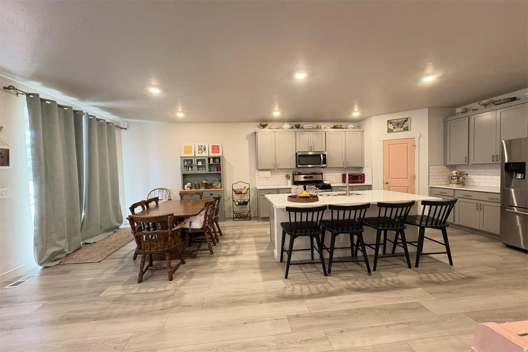 Spacious open-concept living area featuring light wood-finish flooring, a kitchen island with seating, stainless steel appliances, and abundant cabinetry