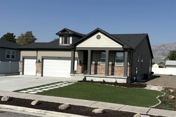 Modern exterior featuring a covered front porch, stone accents, a two-car garage, and a dormer window