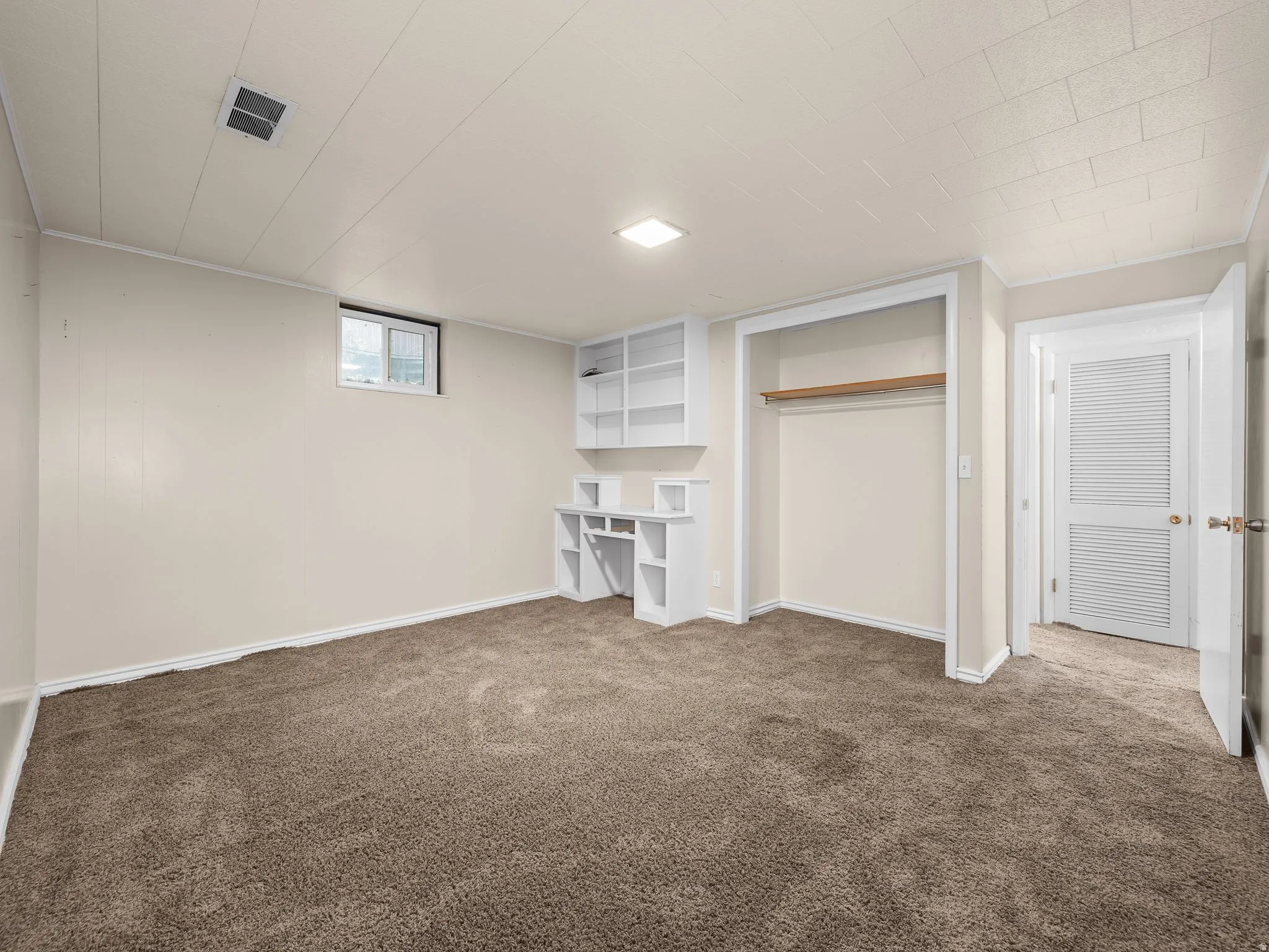 Bedroom 1. Built-in shelving, plush carpeting, built-in desk, and a window
