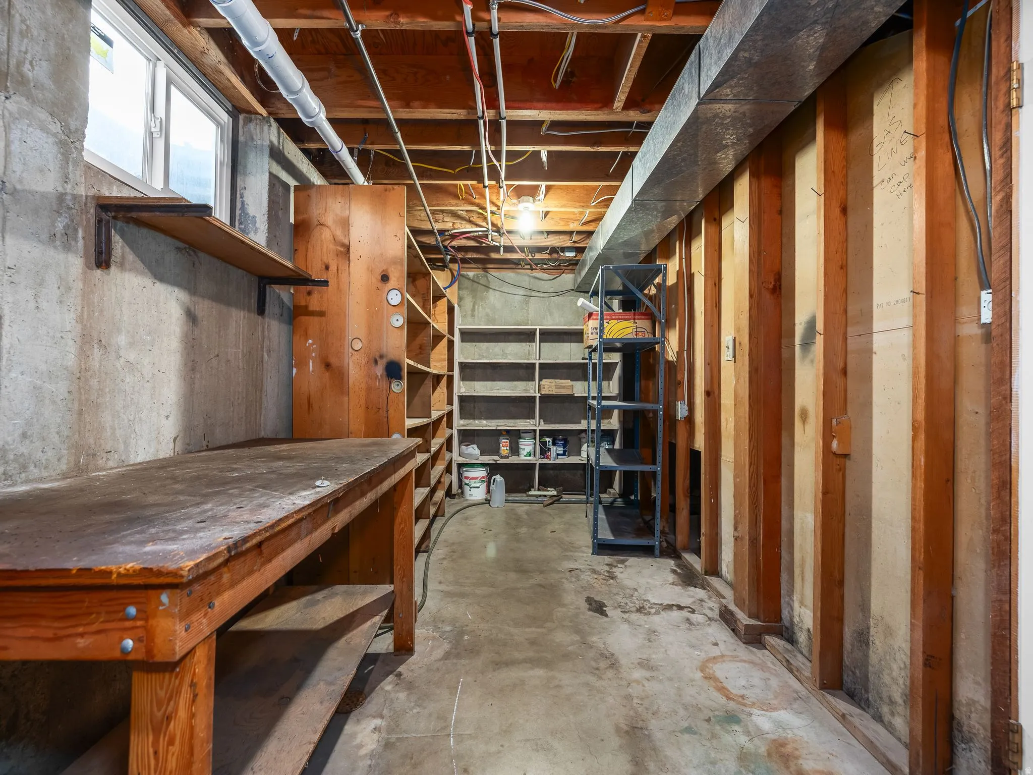Cold storage under the kitchen. Concrete flooring with exposed ceiling joists, wood shelving, and a built-in workbench