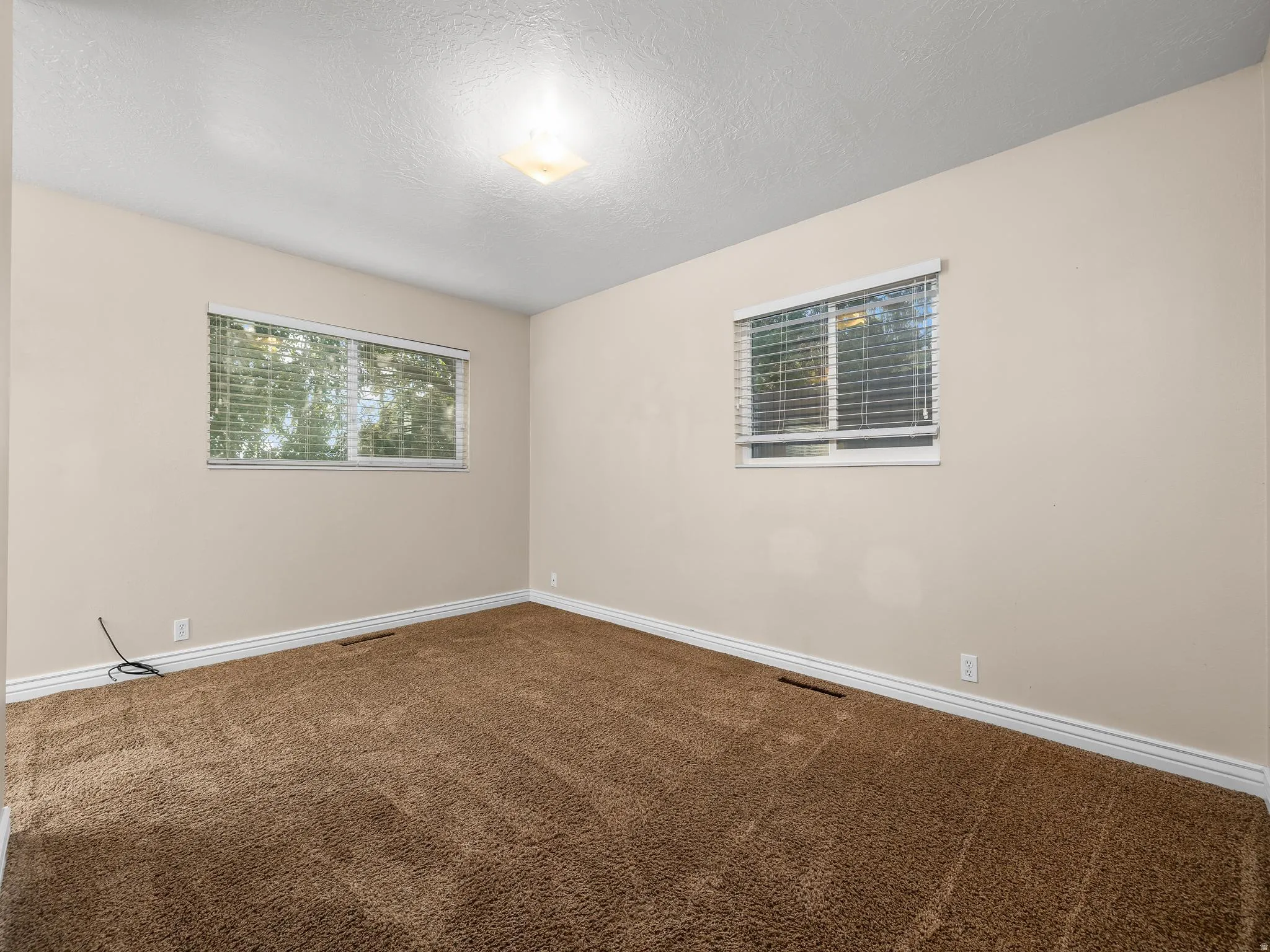 Primary bedroom. Neutral wall paint with two windows providing natural illumination, complemented by recessed lighting
