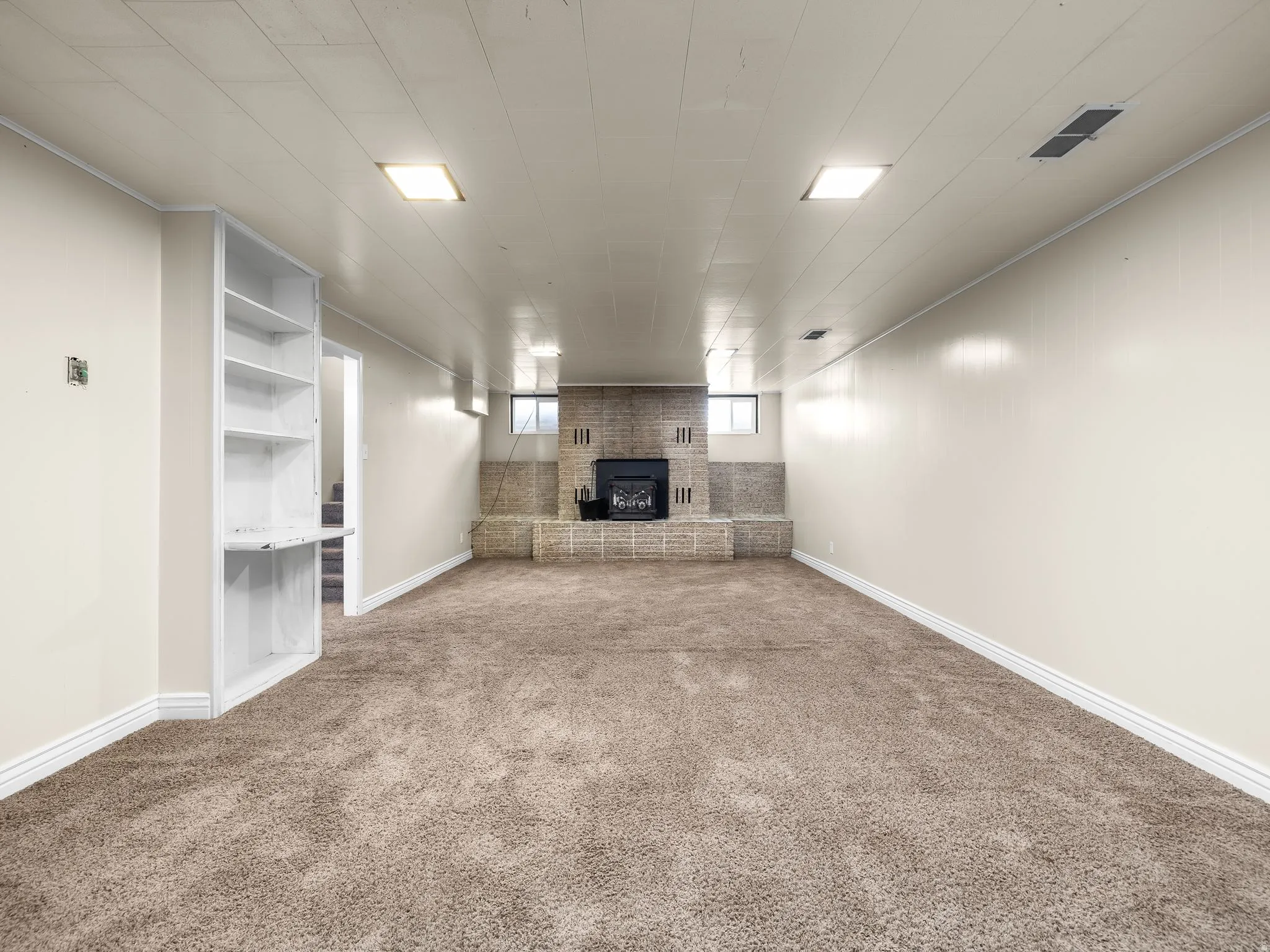 Spacious room featuring carpeting, a brick fireplace with a hearth, built-in shelving, and recessed lighting