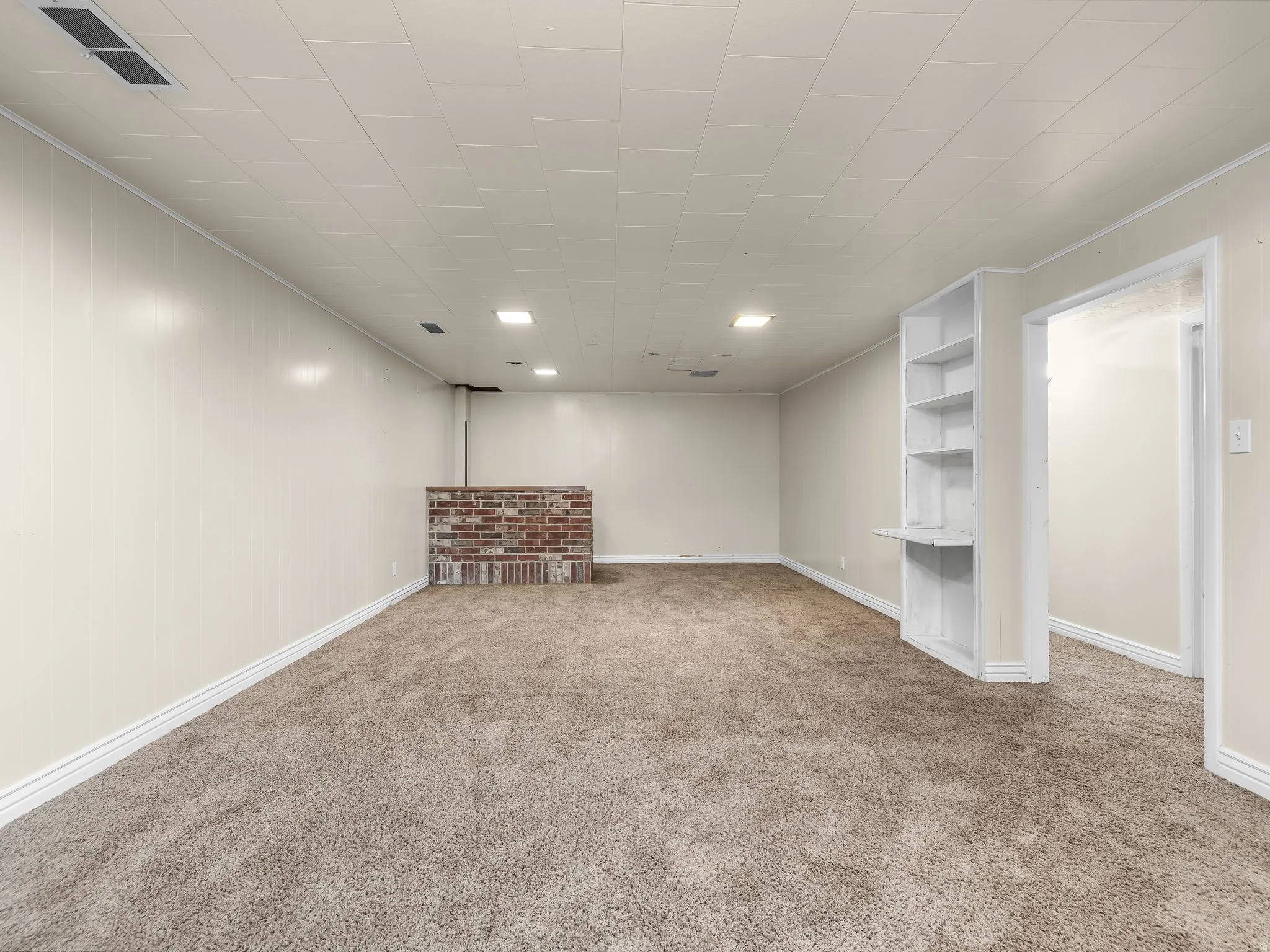 Spacious room featuring neutral carpet, recessed lighting, a built-in shelving unit, and a brick-finish half-wall