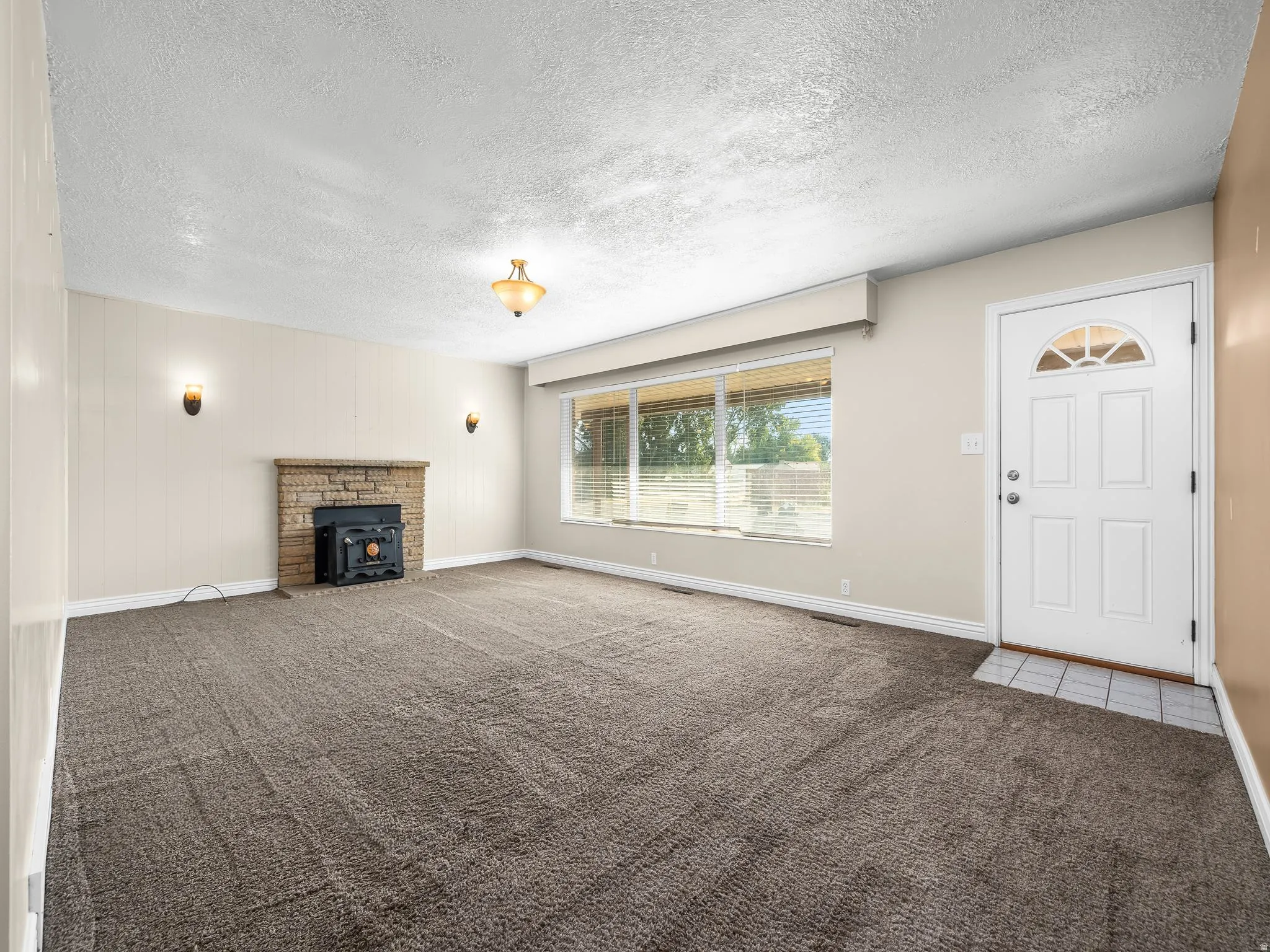 Living area with a stone fireplace, wood-burning stove, large picture window, and a white paneled entry door