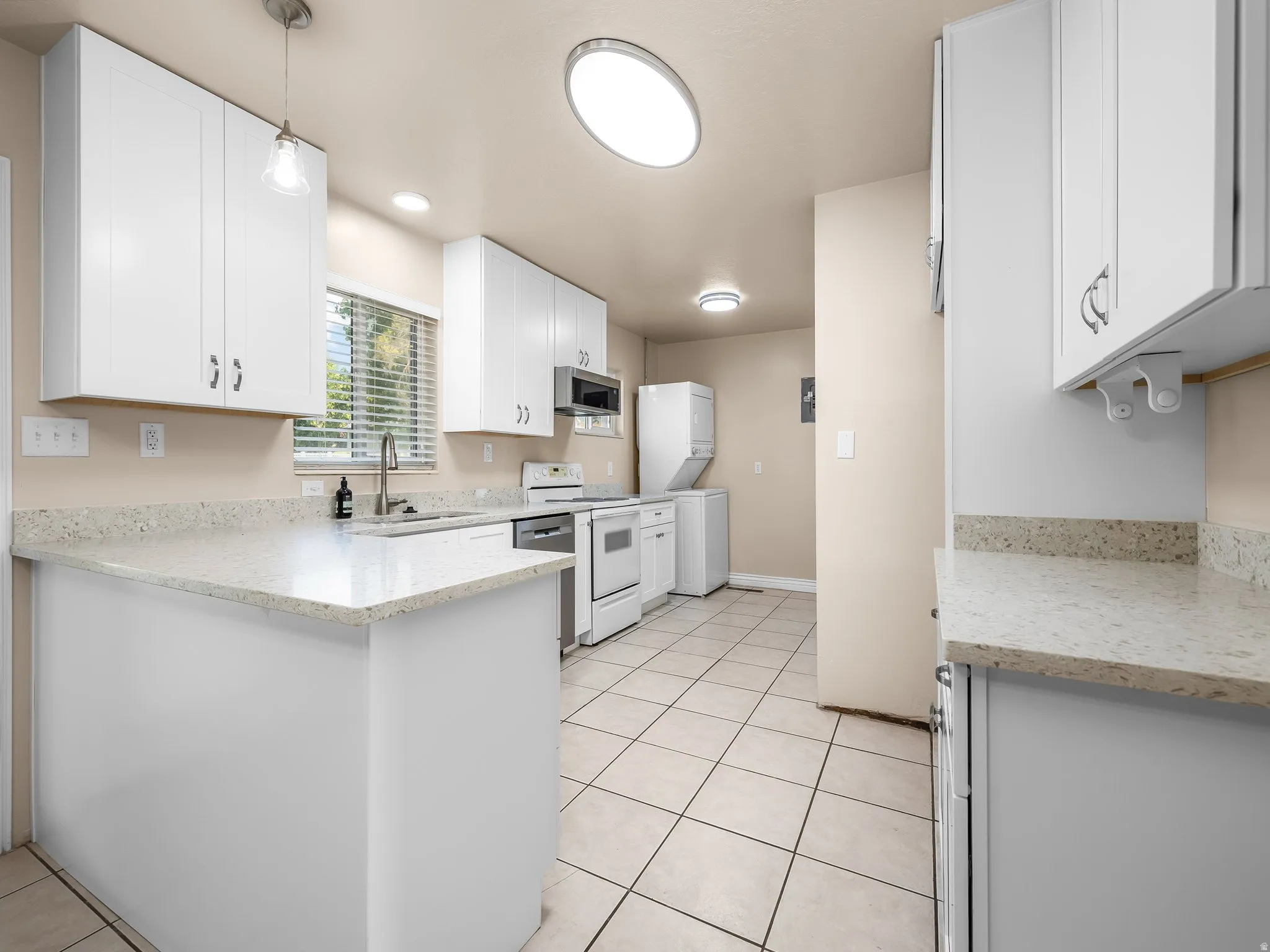 Kitchen featuring white cabinetry, light-toned countertops, a stainless steel sink with a gooseneck faucet, white appliances, and tiled flooring