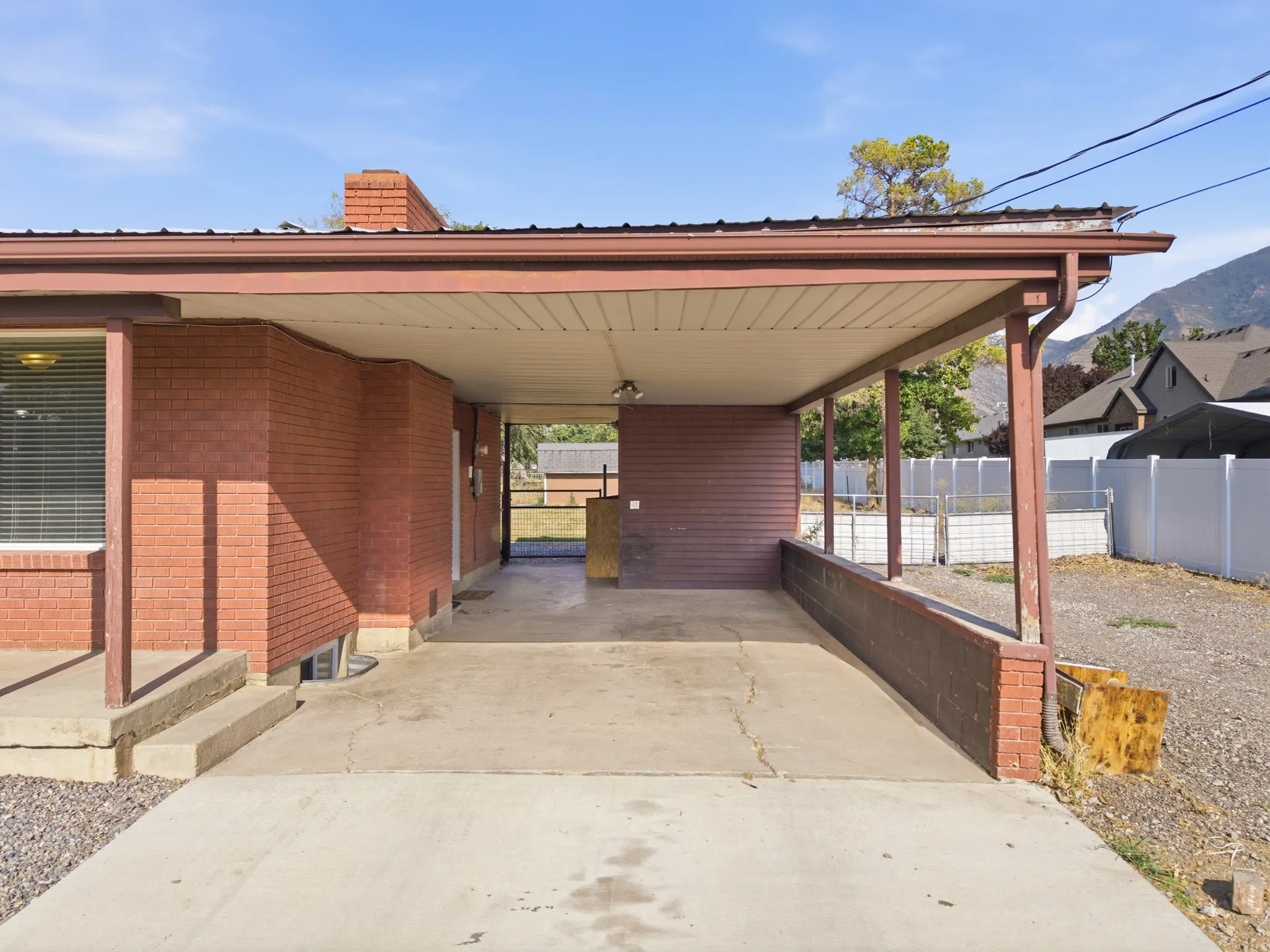 Covered carport with a concrete drive, storage unit, brick exterior, and a metal roof