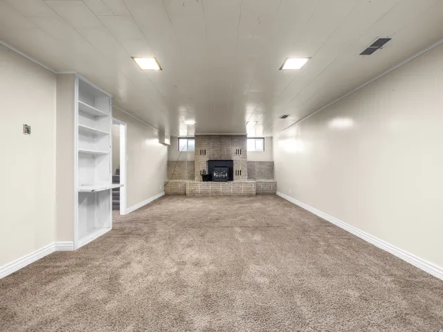 Spacious room featuring carpeting, a brick fireplace with a hearth, built-in shelving, and recessed lighting